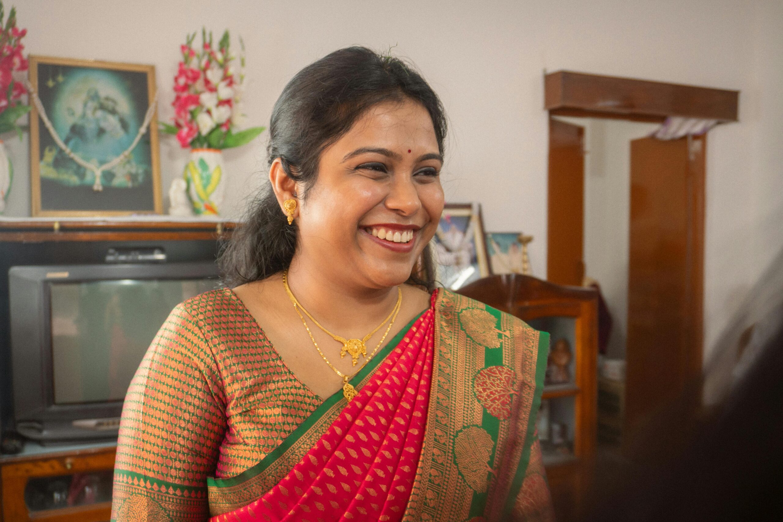 Smiling Indian woman wearing a vibrant saree indoors, capturing traditional elegance and happiness.